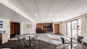 A modern indoor space with a kitchen area, seating arrangements, and a view through large windows. - Motel 6 Great Falls, MT (Great Falls)