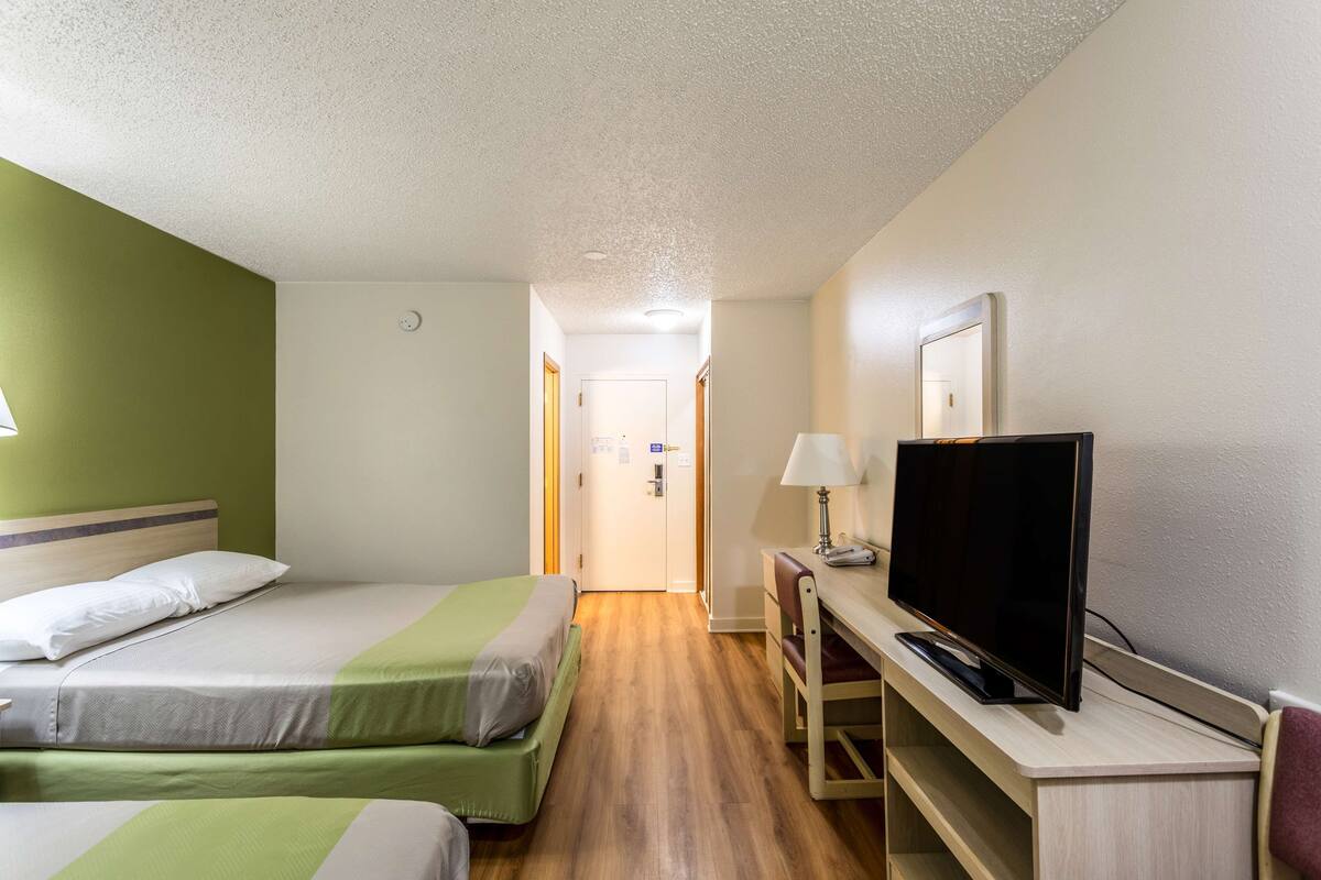 A hotel room with two beds, a TV, a desk, and a lamp.