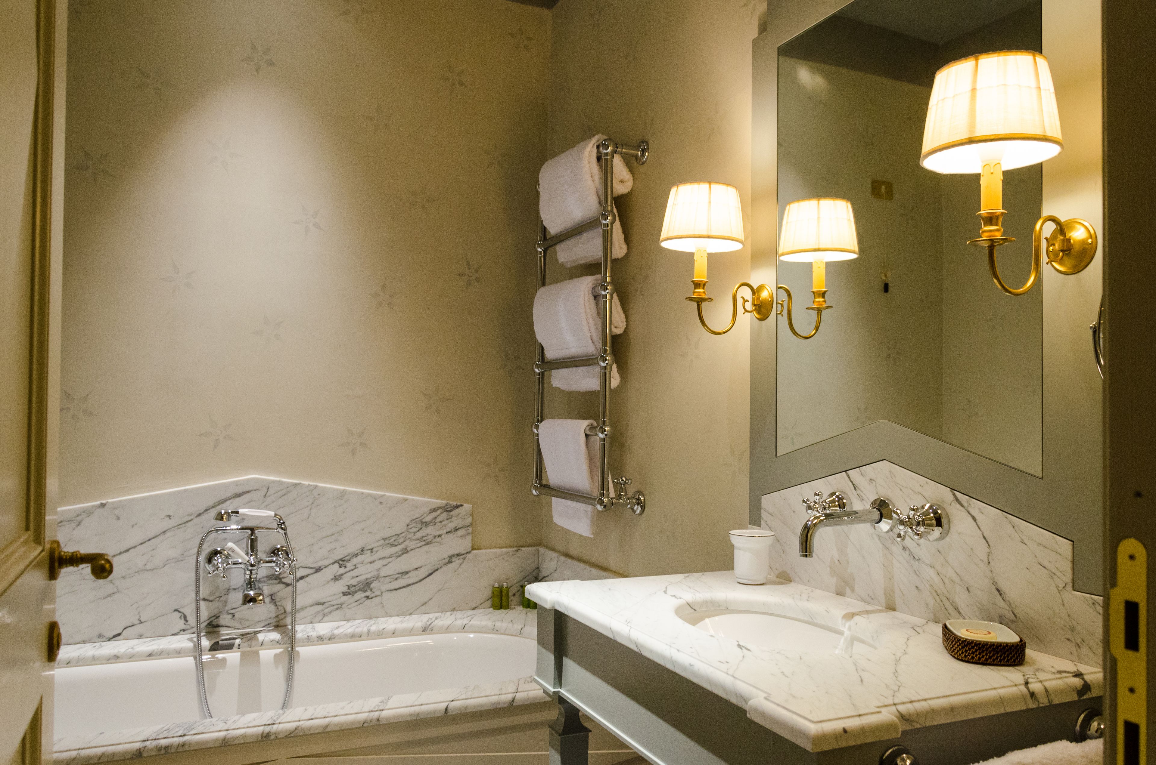 A bathroom with a marble sink, a bathtub, and a towel rack with multiple towels. There are wall-mounted lamps and a large mirror.