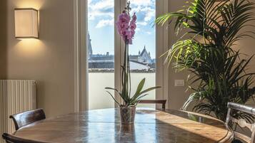 A round dining table with chairs, a potted plant, and a view of a cityscape through large windows.