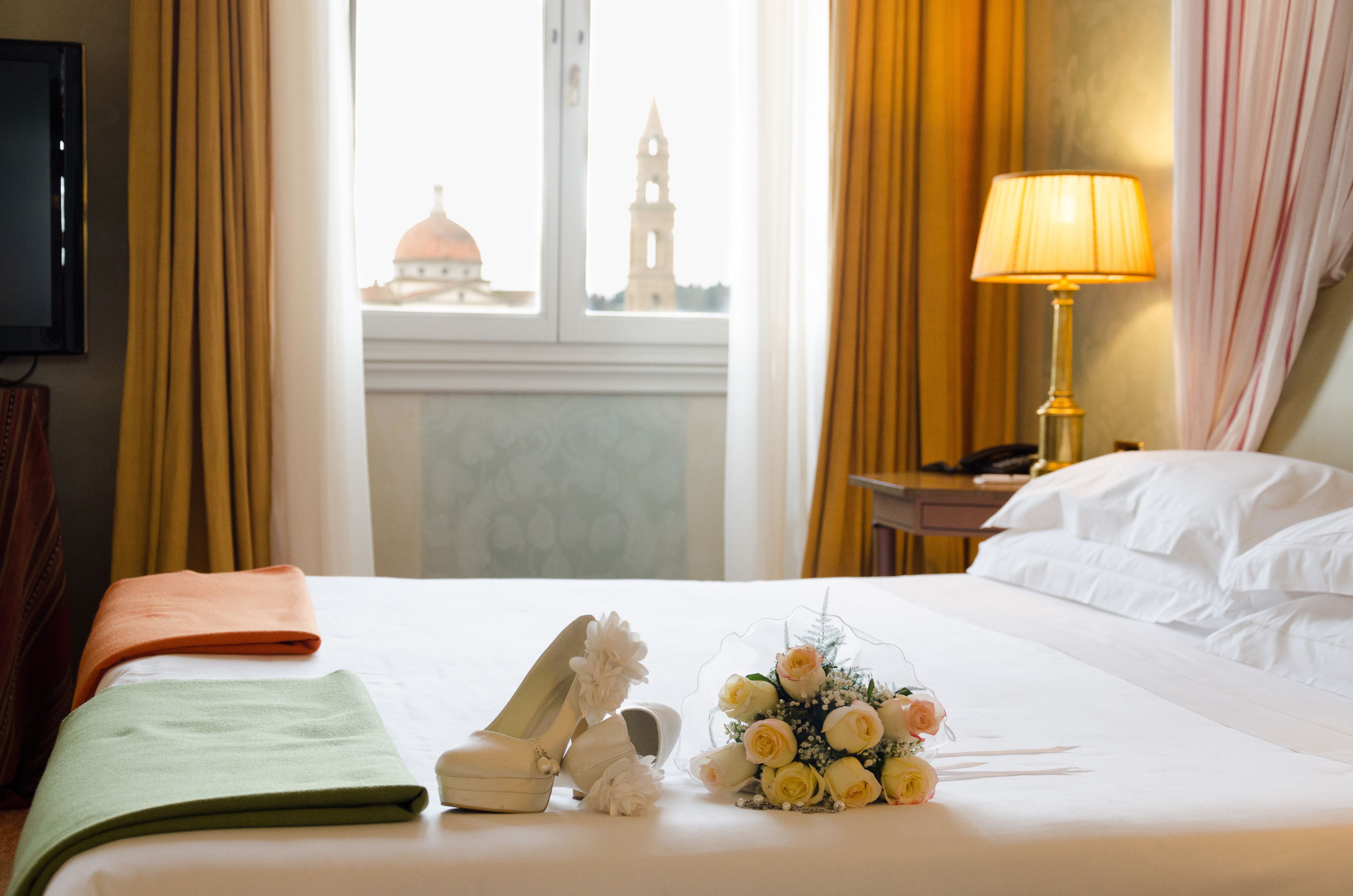 Habitación de hotel con cama, lámpara, un ramillete de flores y vista a un edificio con una torre.