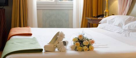 Habitación de hotel con cama, lámpara, un ramillete de flores y vista a un edificio con una torre.