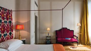 Habitación de hotel con cama con dosel, una silla, dos lámparas y cortina estampada.