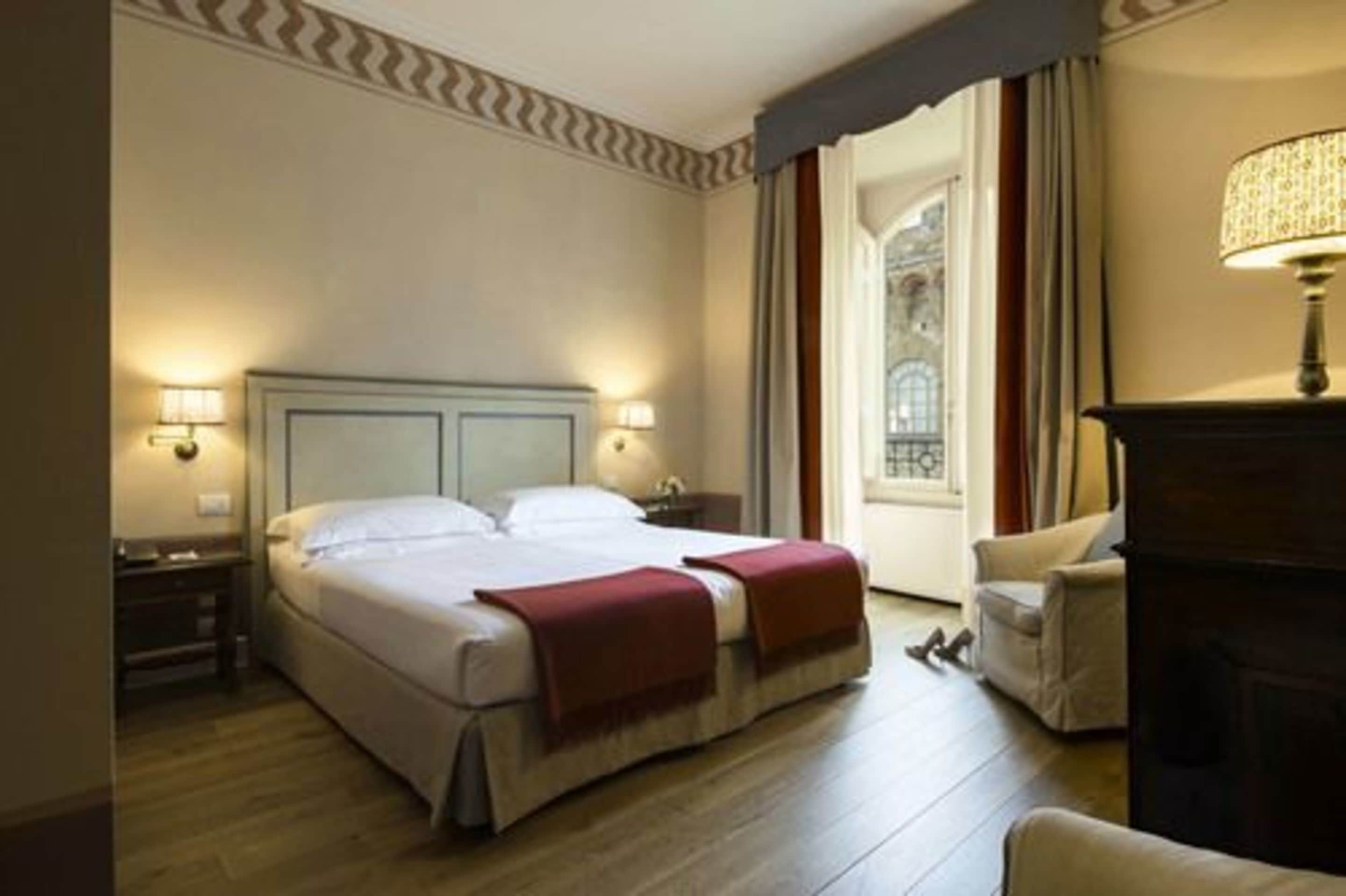 Una habitación de hotel con una cama grande, dos lámparas de noche, una silla y una chimenea.