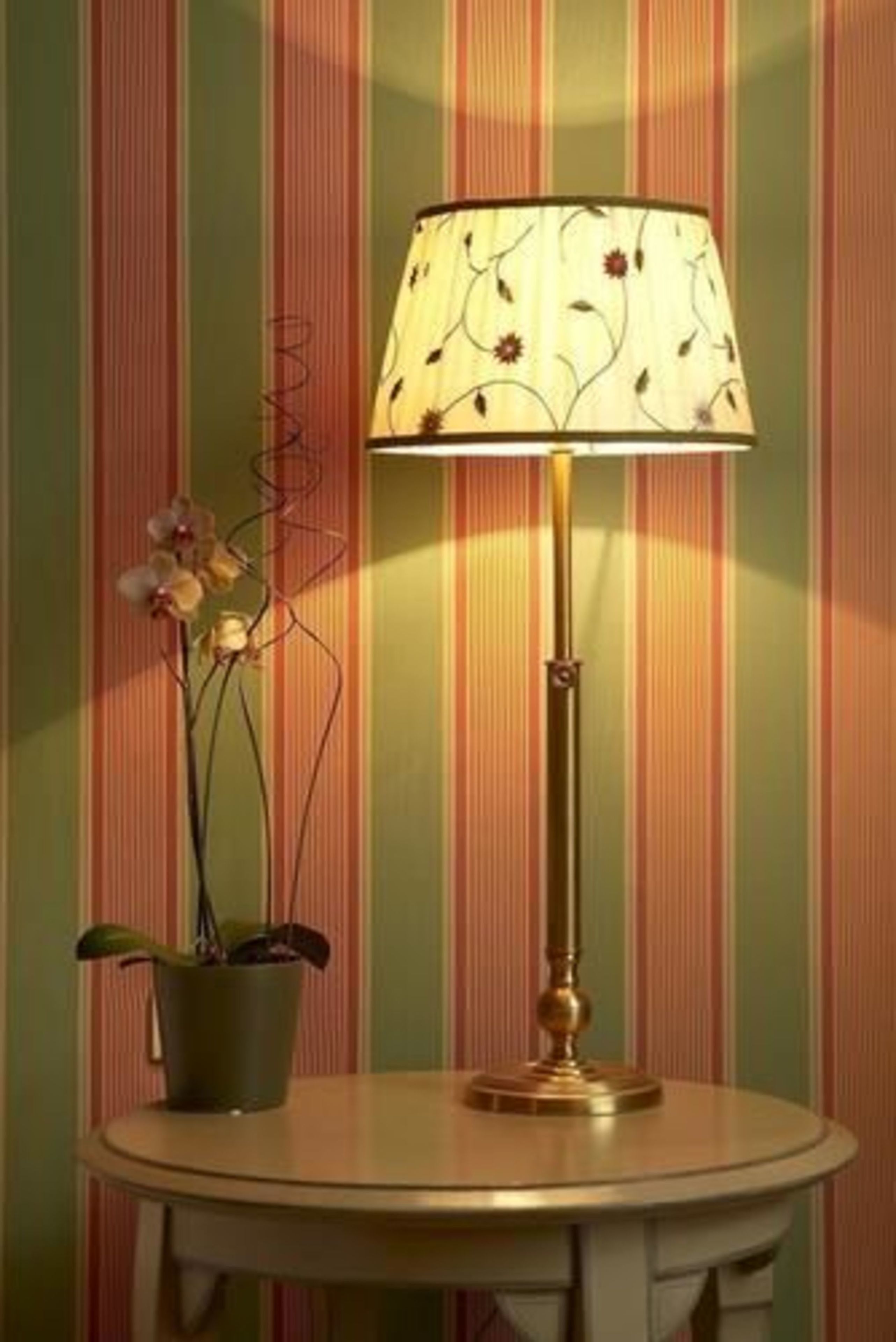 A round table with a lamp and a potted plant against a striped wall.