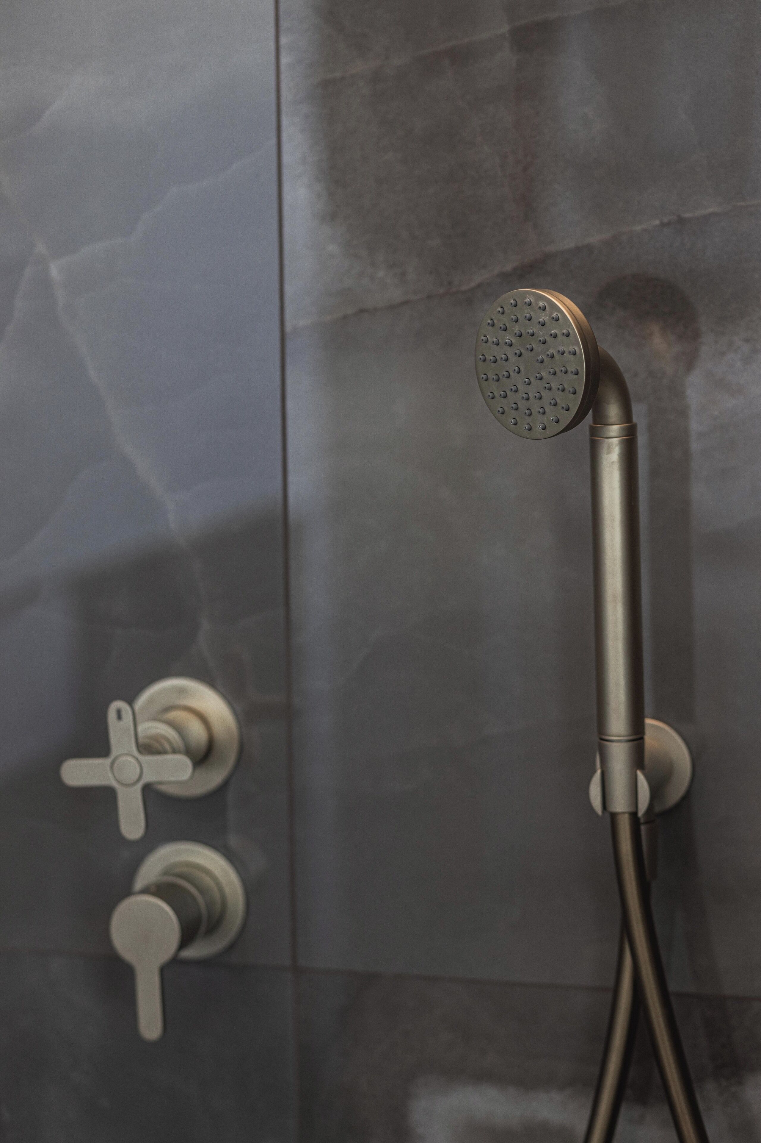 A showerhead with a round, perforated design, a vertical handle, and a flexible hose.