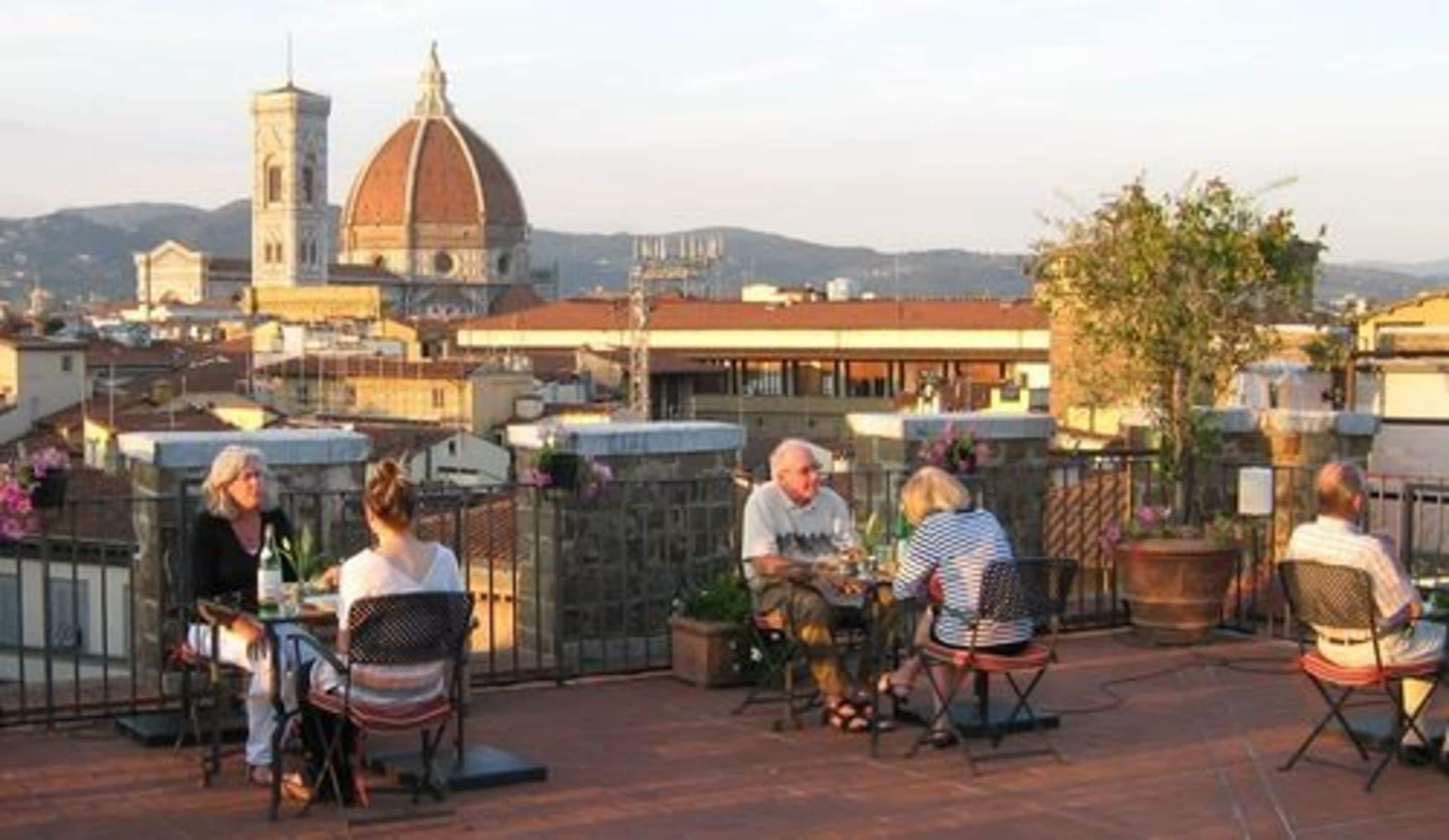 A group of people seated on outdoor patio chairs with a cityscape and a prominent dome-shaped building in the background.