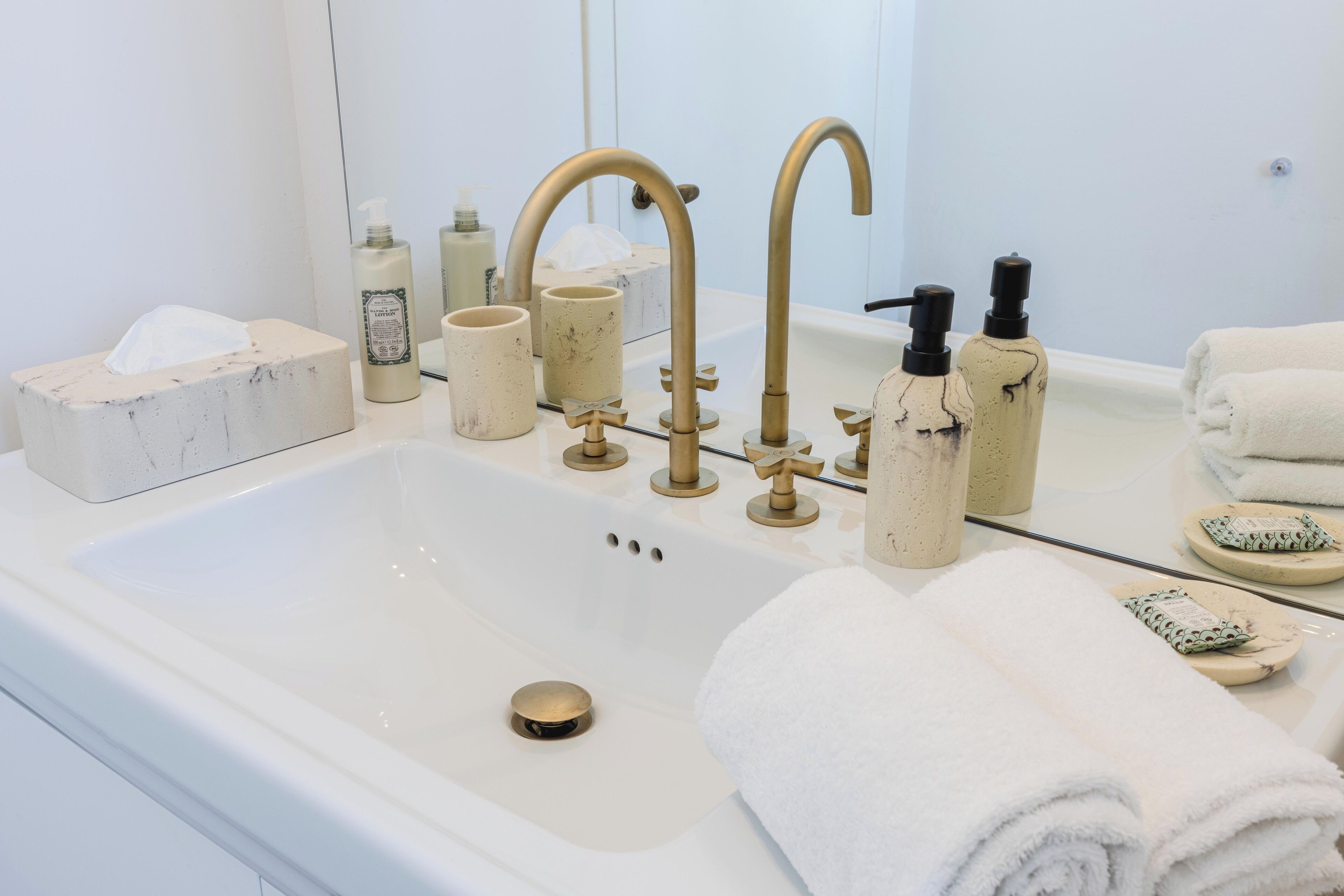 A bathroom with a white sink, two gold faucets, a tissue box, a soap dispenser, and a towel rack.