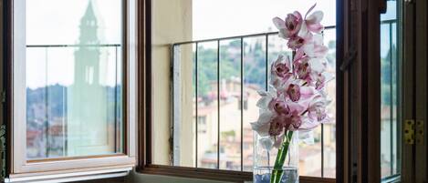 Una ventana con vistas a un edificio y un florero con flores en el alféizar.