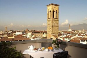 Un balcon avec une table dressée pour le petit-déjeuner, offrant une vue sur un paysage urbain avec des bâtiments historiques et une tour imposante.