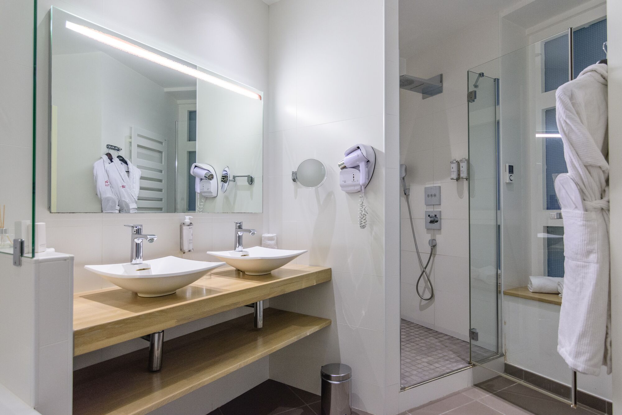 Un baño moderno con dos lavamanos, un espejo grande, un secador de pelo y una ducha con mampara de cristal.