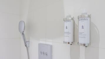 A bathroom with a shower, a handheld showerhead, and two bottles of Sothys Paris shampoo and conditioner on a shelf.