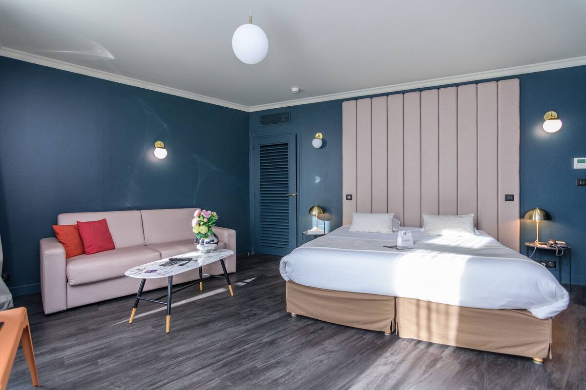 Una habitación de hotel moderna con una cama, un sofá, una mesita de centro y un televisor montado en la pared.