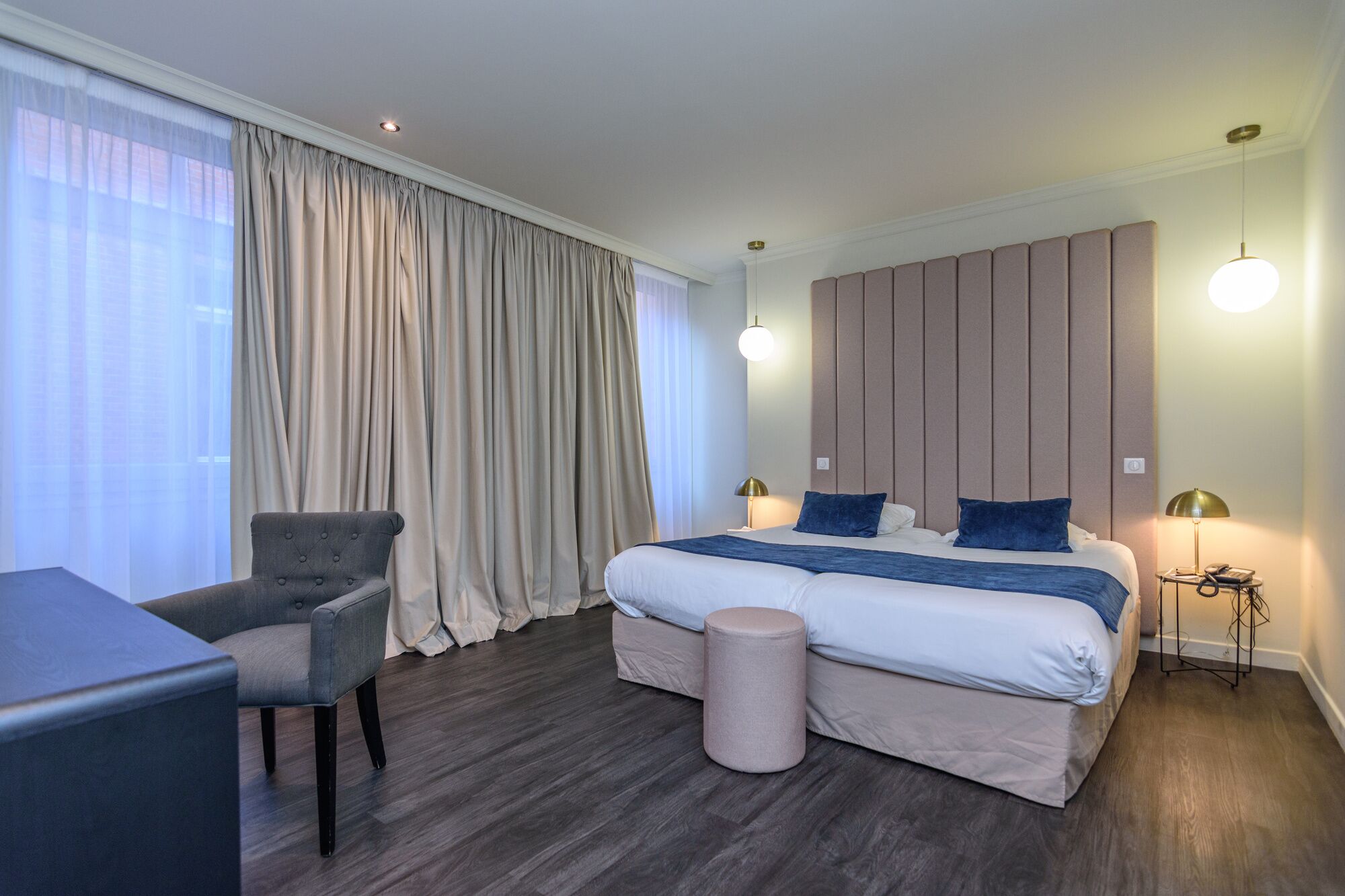 A modern hotel room with a large bed, a chair, a small table, and a bedside lamp.