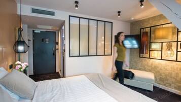 Quarto de hotel moderno com cama, sofá, televisão e uma parede decorativa.