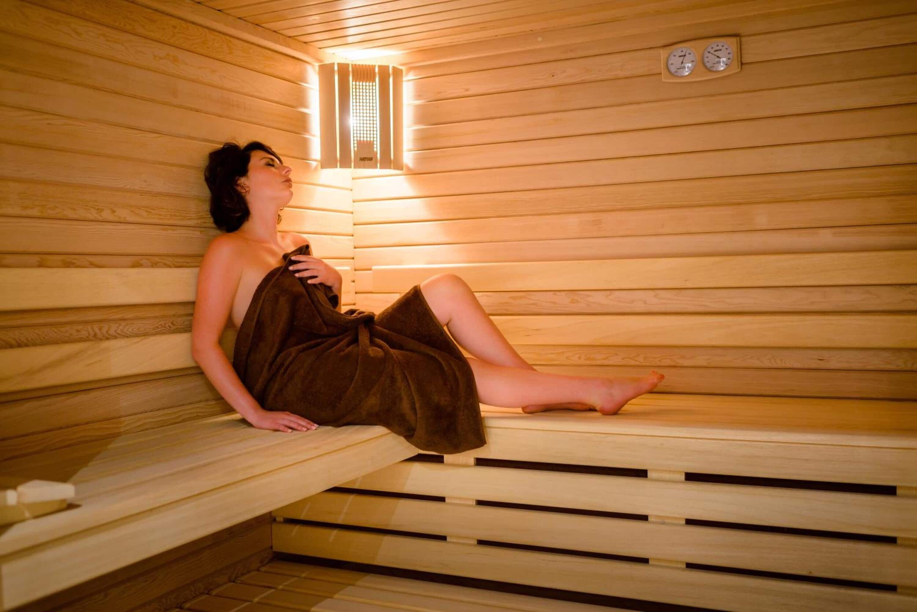 A person sitting in a wooden sauna with a bench and a small window.