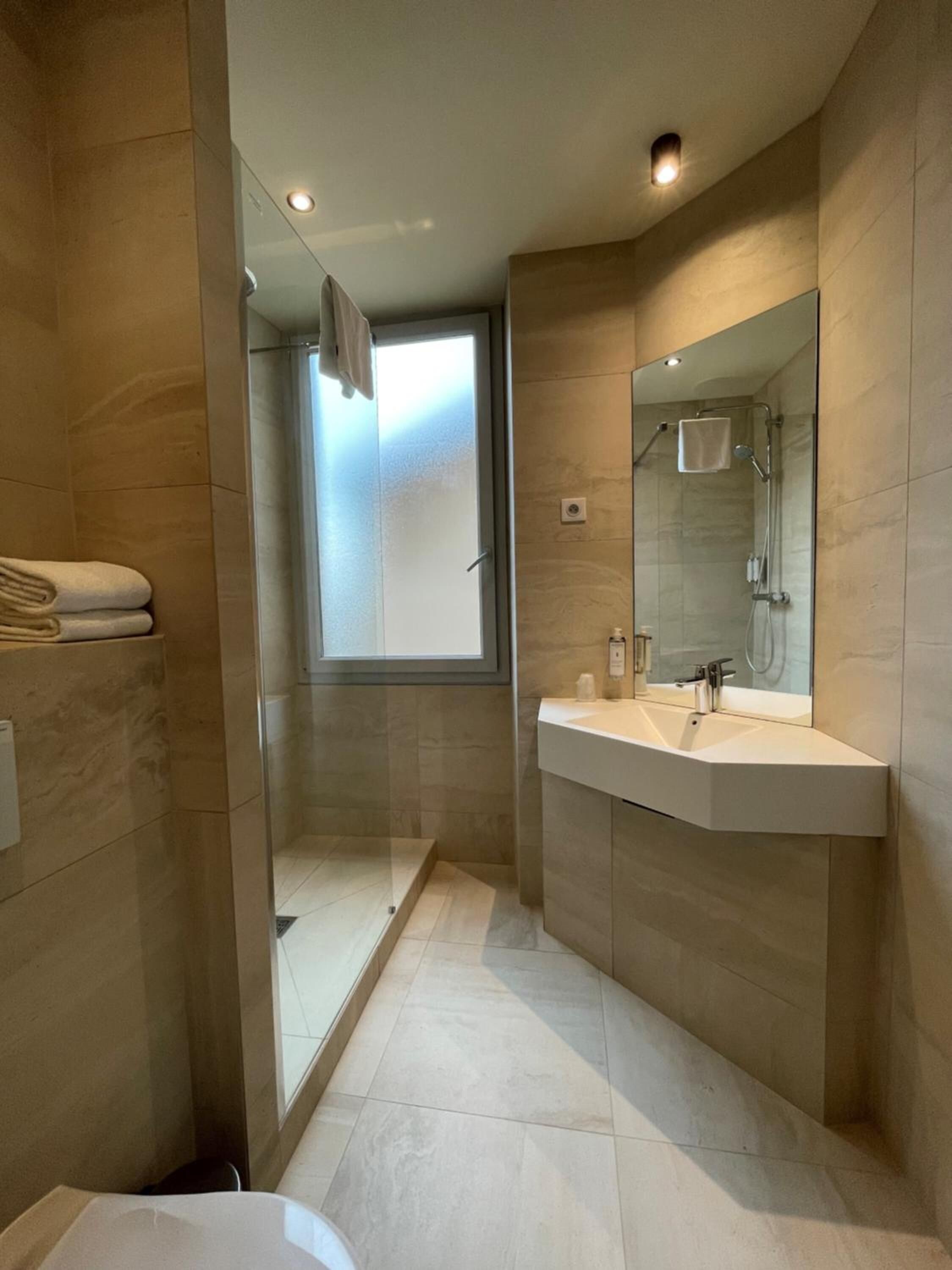 A modern bathroom with a glass shower enclosure, a large mirror, and a white sink.