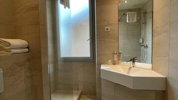 Un baño moderno con cabina de ducha de vidrio, un espejo grande y un lavabo blanco.