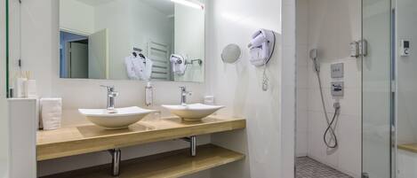A modern bathroom with two sinks, a large mirror, a hairdryer, and a glass-enclosed shower area.