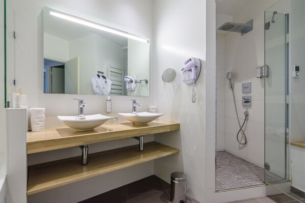 A modern bathroom with two sinks, a large mirror, a hairdryer, and a glass-enclosed shower area.