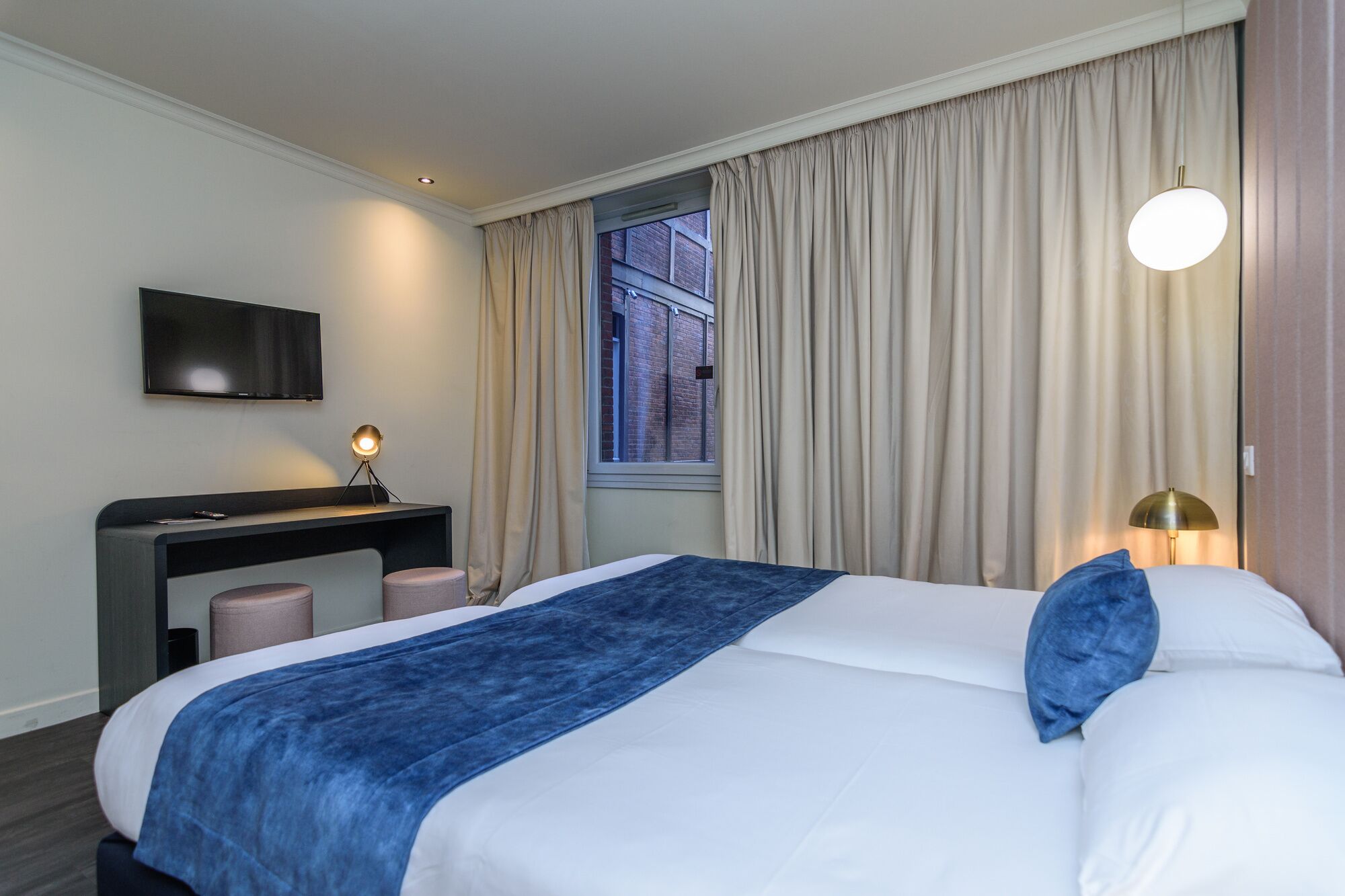 A hotel room with a bed, a desk, a TV, and a window with curtains.