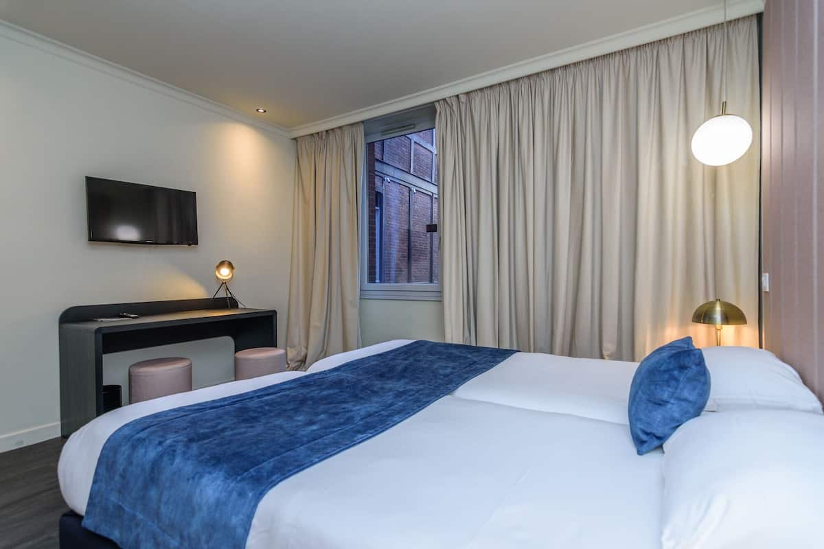 A hotel room with a bed, a desk, a TV, and a window with curtains.