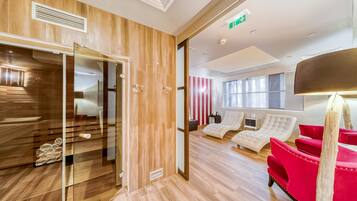 Een moderne hotel lobby met een houten vloer, een glazen deur naar een kamer en een zithoek met rode en witte stoelen.