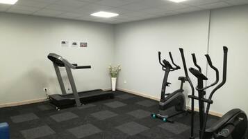 Une salle de remise en forme équipée d’un tapis de course, d’un vélo elliptique et de vélos d’appartement.