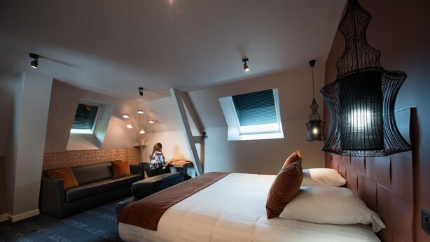 A modern hotel room with a large bed, a sofa, a desk, and a window with blinds. - Le Saint-Georges Hotel & Spa (Chalon-sur-Saone)