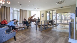 Un vestíbulo amplio con un piano de cola, asientos cómodos y ventanas grandes que ofrecen vistas al exterior.