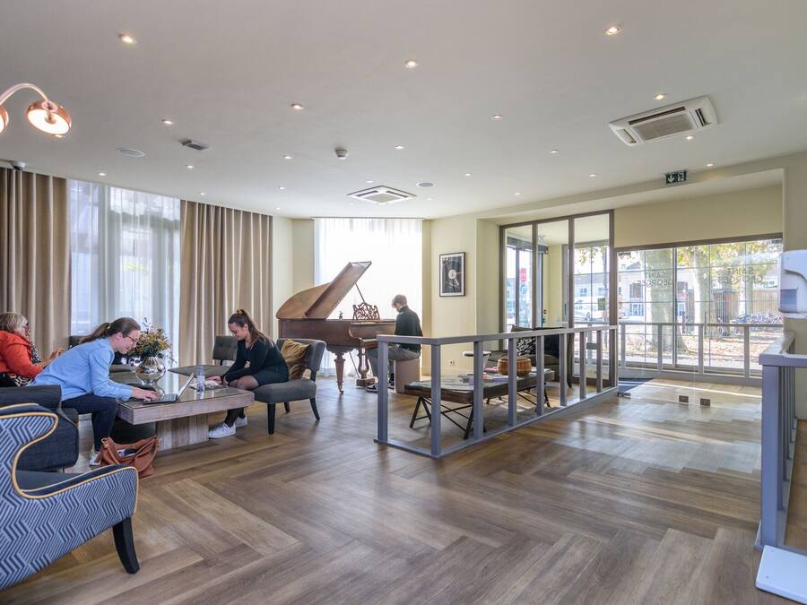 Un'ampia hall con un pianoforte a coda, comodi posti a sedere e grandi finestre che offrono vista all'esterno.