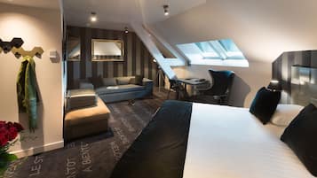 A modern hotel room with a large bed, a desk, a chair, a sofa, and a skylight.