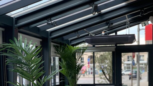 Interior de restaurante con cabinas de madera, plantas en macetas y vista de la calle a través de amplios ventanales.