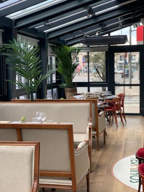 A restaurant interior with wooden booths, potted plants, and a view of the street through large windows.
