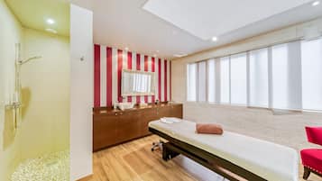 Une salle de spa moderne avec un plancher en bois, une table de massage, un grand miroir et une fenêtre avec des rideaux.