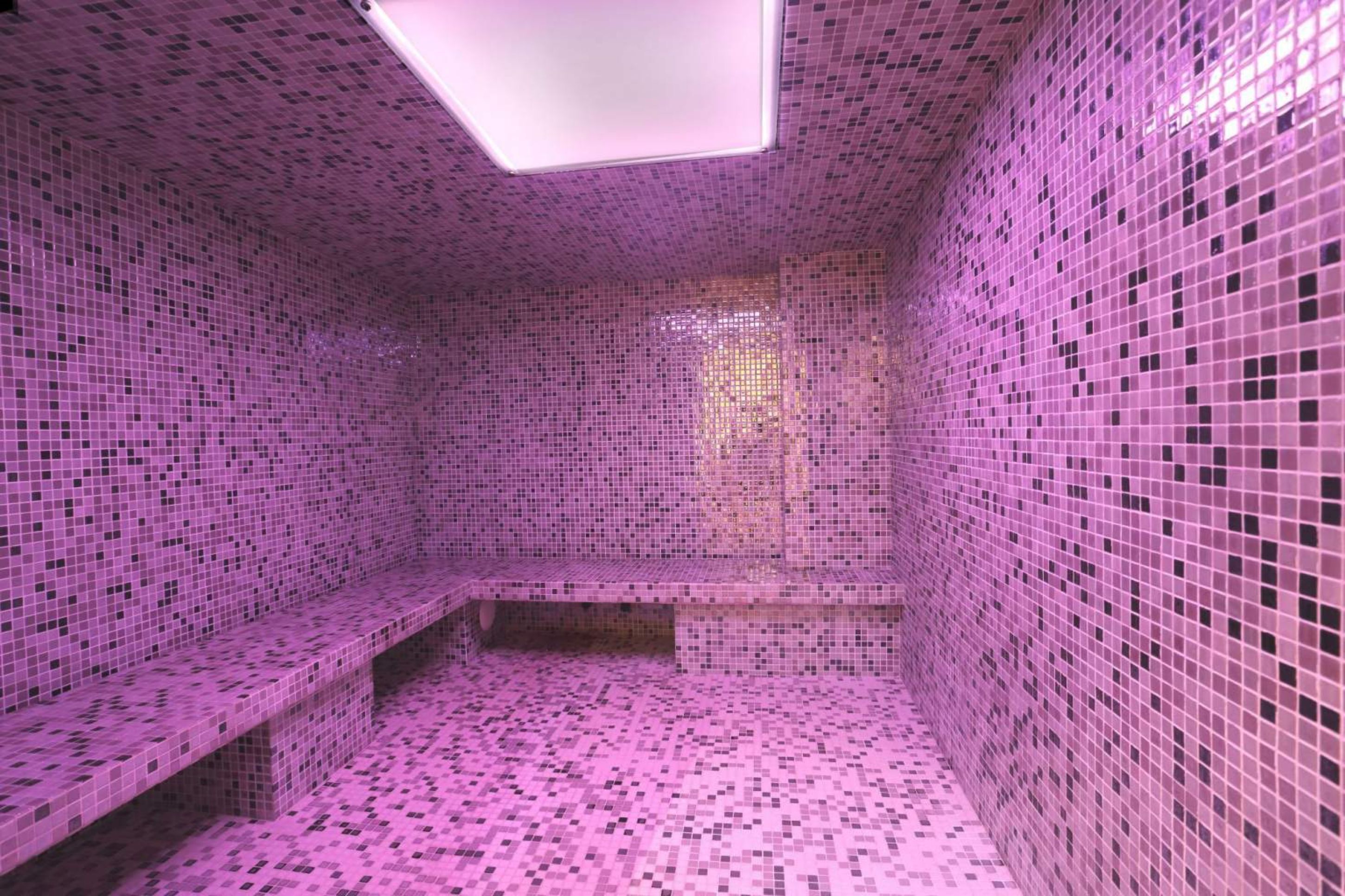 Una habitación con paredes y suelo de mosaico rosa, un banco y un tragaluz.