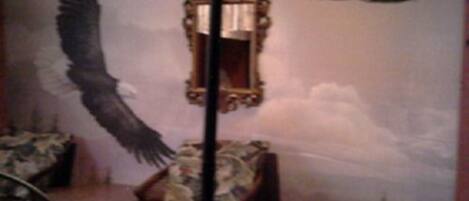 Quarto com um grande mural de águias em voo, um espelho e uma cadeira.