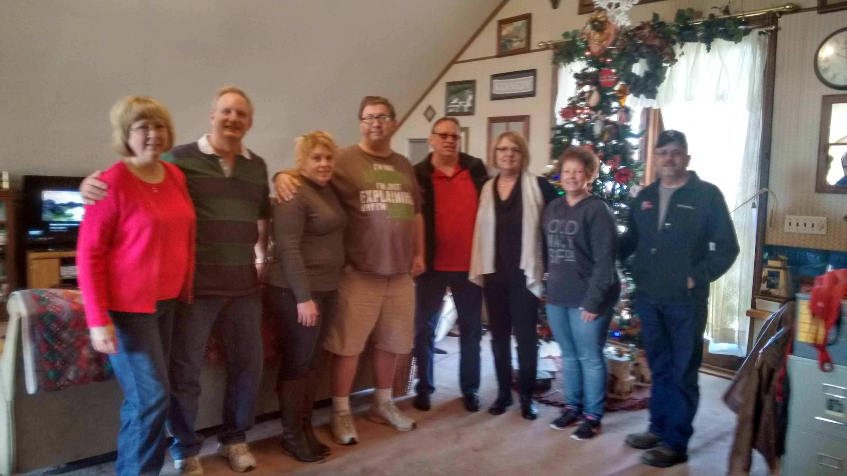 A group of people standing in a living room with a Christmas tree in the background.