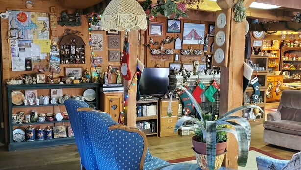 A cozy, wooden-floored room with a blue patterned chair, a round glass table, and a variety of decorative items and knick-knacks on shelves and walls. - Kennedys Red Barn Inn (Perry)