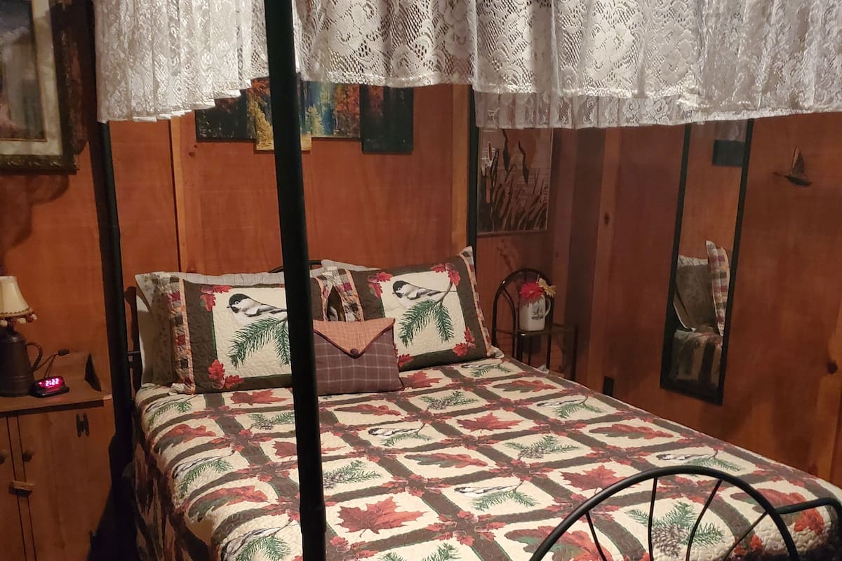 A bed with a metal frame and a canopy, a wooden nightstand with a lamp, and a wall with a framed picture.