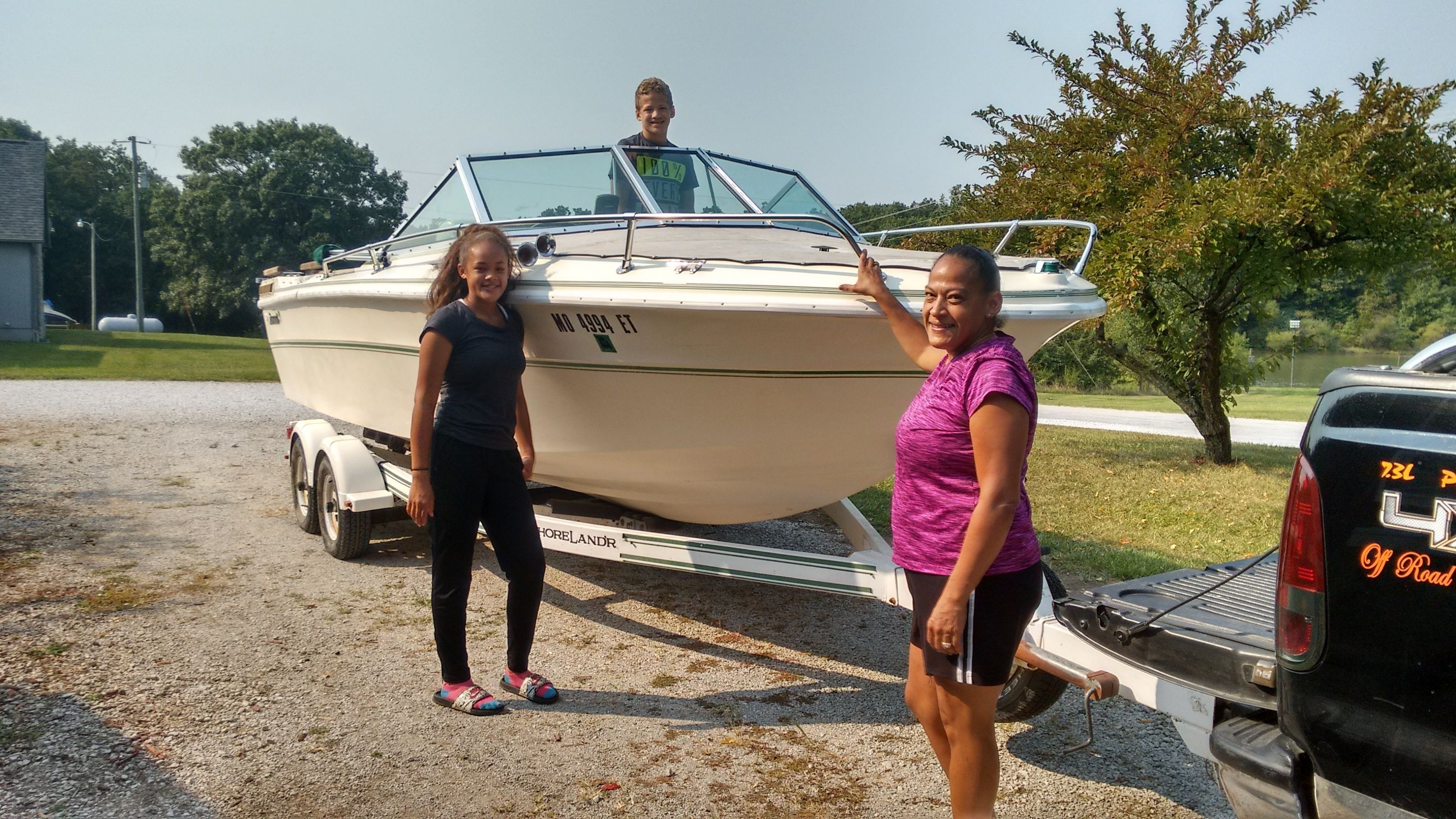 A boat on a trailer with two people standing beside it.