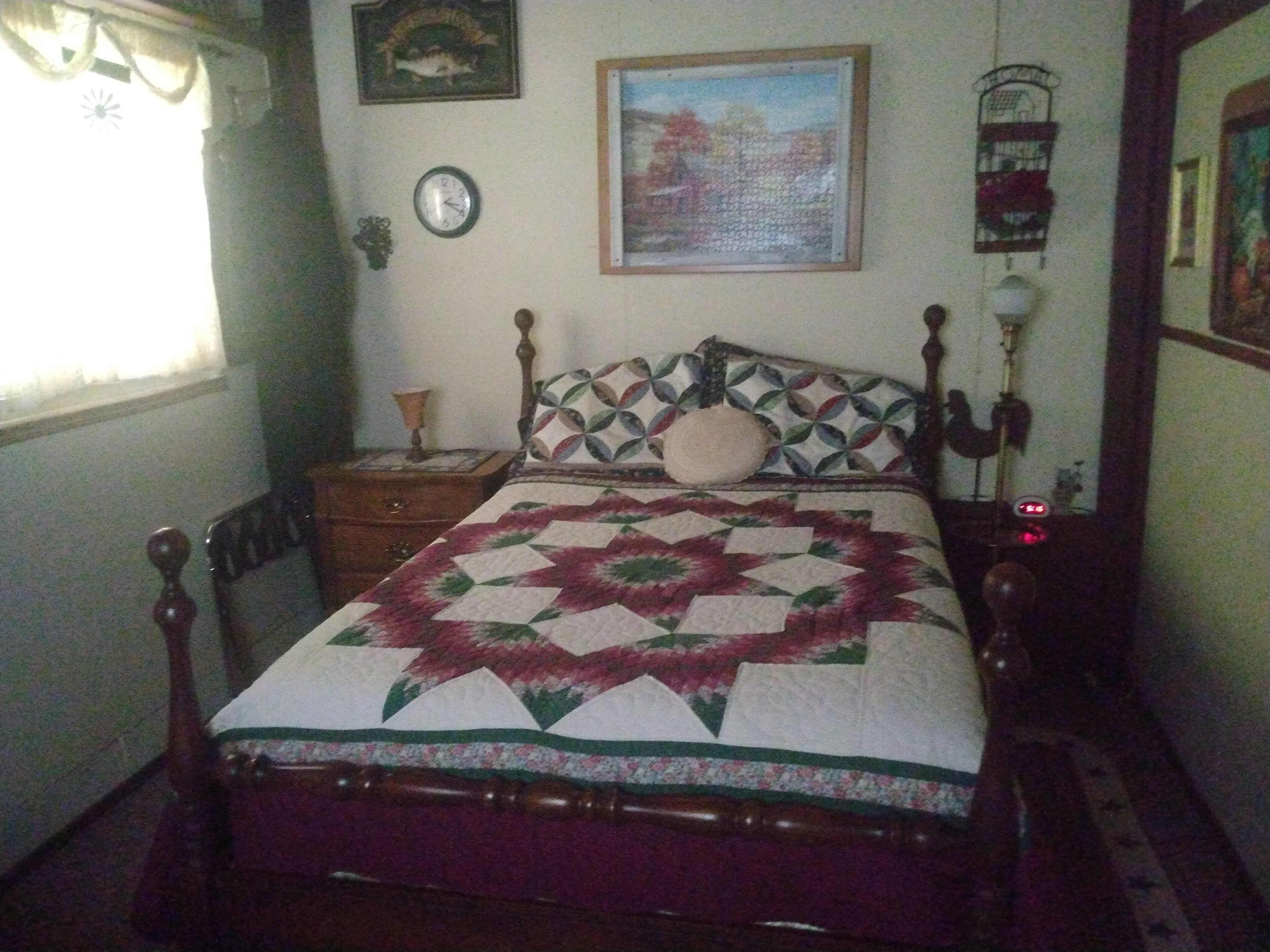 A bedroom with a wooden bed, a nightstand, a wall clock, and a framed painting.