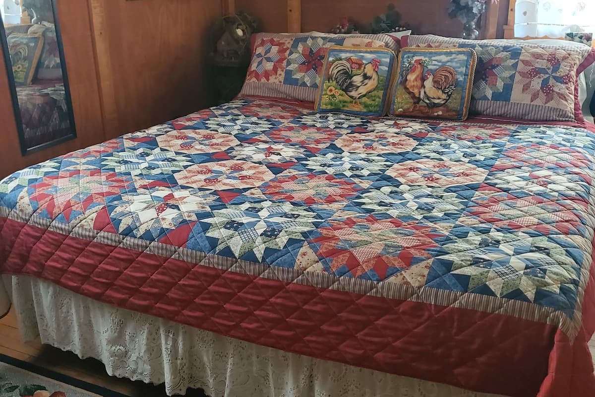 A bed with a colorful quilt, a floral rug, and wooden walls.
