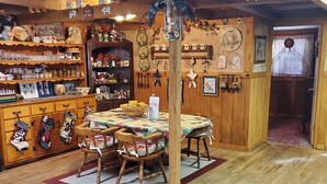 A cozy, rustic room with wooden floors and furniture, a dining table with chairs, and shelves filled with various items. - Kennedys Red Barn Inn (Perry)