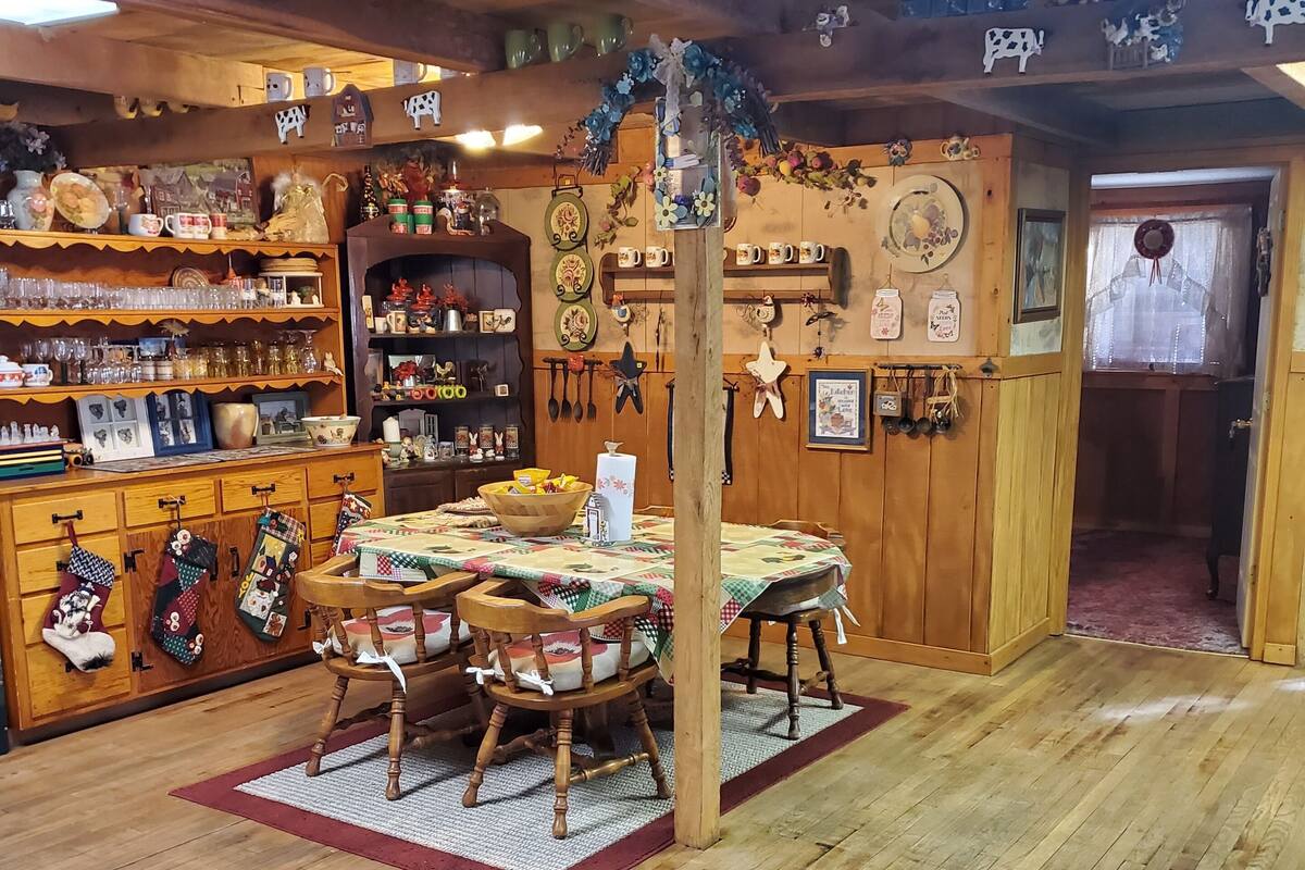 A cozy, rustic room with wooden floors and furniture, a dining table with chairs, and shelves filled with various items.