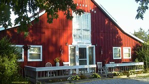 A red barn with a porch and white chairs, labeled "VACANCY". - Kennedys Red Barn Inn (Perry)