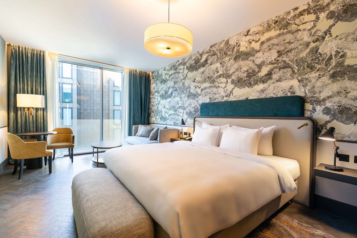 A modern hotel room with a large bed, a desk, and a seating area.