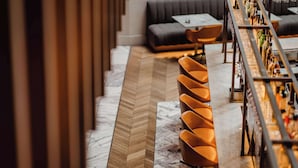Un espace bar doté d’un long comptoir, de chaises orange et d’un sol à motifs en chevrons.