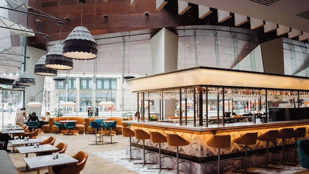 Un espace bar moderne doté d’un comptoir en marbre et de nombreux sièges, notamment des tabourets de bar et des tables.