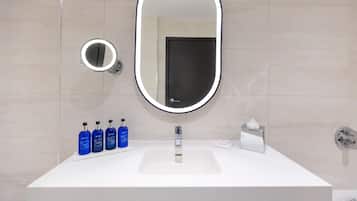 Un baño con un lavabo blanco, un espejo ovalado grande con luz y cuatro botellas azules sobre la encimera.